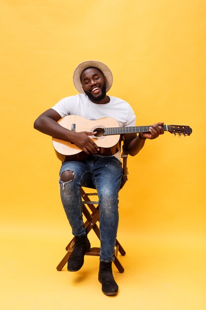 Foto completo do homem artístico animado tocando seu violão. Isolado em fundo amarelo.