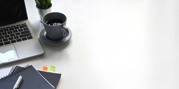 Foto de la computadora portátil, la taza de café, el cuaderno, el diario, la pluma, la planta en maceta que pone en el escritorio de trabajo blanco. Concepto de lugar de trabajo ordenado.