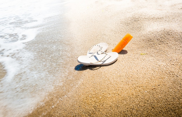 Foto conceitual de chinelos e protetor solar na praia arenosa