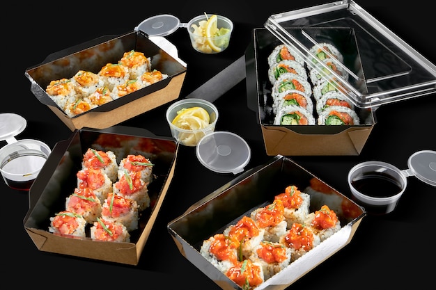 Foto conceitual para entrega de rolo de sushi. Rola em embalagens de papelão sobre uma superfície preta. 3 tipos de pães picantes com salmão, vieiras e atum, pãezinhos com salmão e cebola