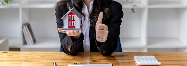 Foto de concepto de una mujer sosteniendo un modelo de un concepto de casa pequeña para comprar una casa o bienes raíces, ella es vendedora de bienes raíces y tiene una casa modelo en el proyecto. Comercio de bienes raíces.