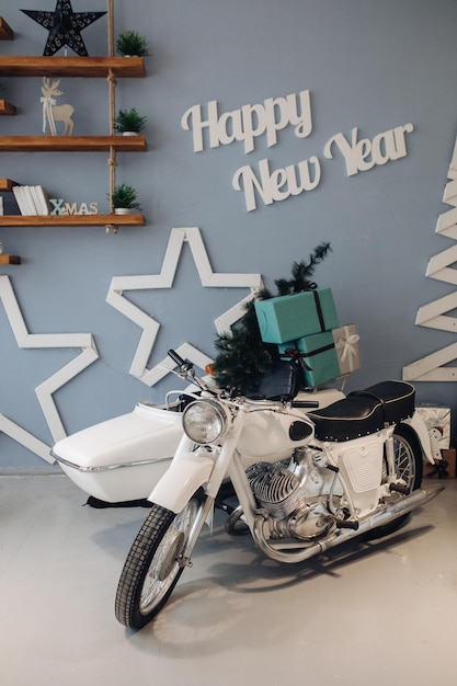 Foto conservada em estoque da motocicleta branca com árvore de Natal em miniatura e presentes de Natal embrulhados no berço. Interior atmosférico para o dia de Natal. Ano Novo de 2020.