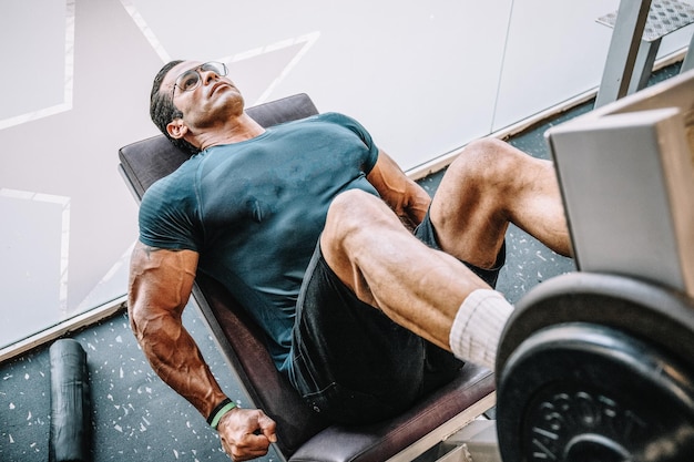 Foto conservada em estoque de um homem musculoso treina pernas na máquina de ginástica Fitness