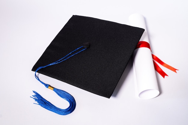 Foto conservada em estoque de uma placa de argamassa de formatura e certificado de diploma isolado no fundo branco com espaço de cópia negativa para adicionar texto. Chapéu de formatura com diploma na mesa contra fundo branco