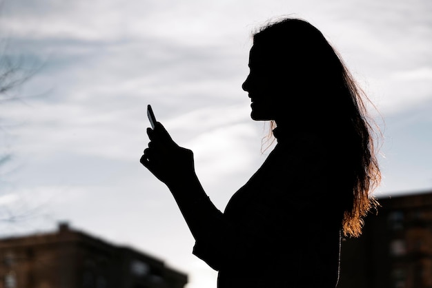 Foto conservada em estoque de uma vista lateral de uma jovem mulher de negócios nas sombras. Ela está enviando mensagens de texto.