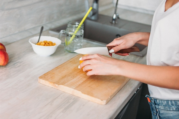 La foto de la cosecha de la mujer joven de la muchacha delgada corta el limón en cocina