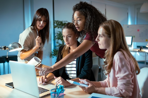 Foto de cuatro empresarias inteligentes hablando y revisando el último trabajo realizado en la computadora en un espacio de trabajo conjunto.