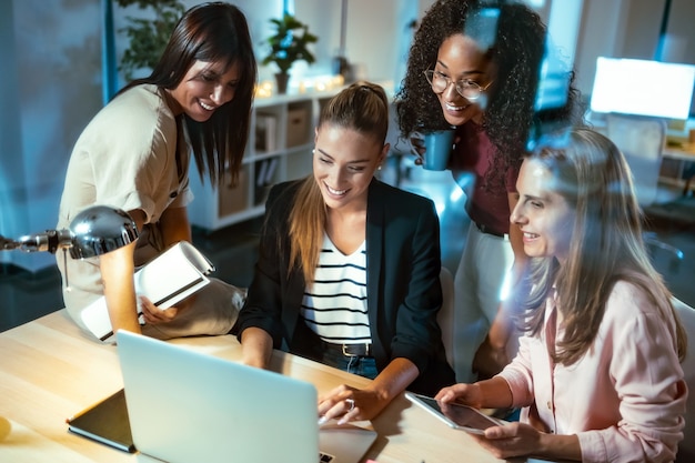 Foto de cuatro empresarias inteligentes hablando y revisando el último trabajo realizado en la computadora en un espacio de trabajo conjunto.