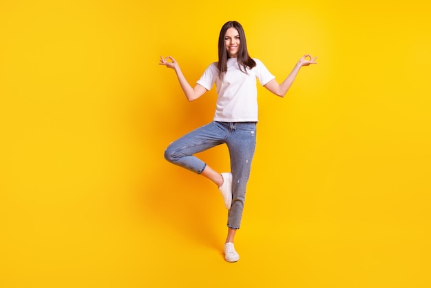 Foto de cuerpo completo de una joven encantadora que medita tranquilamente con ropa informal aislada sobre un fondo de color amarillo