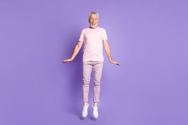 Foto de cuerpo entero del anciano saltar palmas infantiles usar camiseta rosa pantalones zapatillas de deporte aislado fondo de color violeta