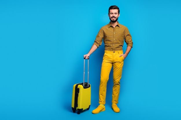 Foto de cuerpo entero de un chico alegre positivo que tiene un gran carro de bolsa brillante disfruta del turismo el fin de semana usa un buen look ropa de moda gumshoes aislados sobre color azul