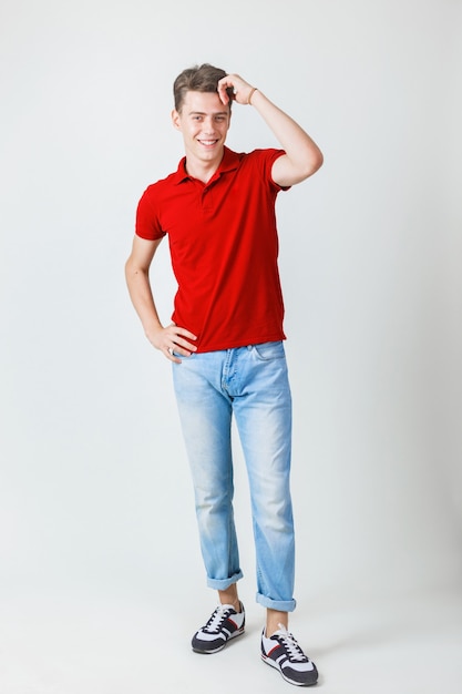 Foto de cuerpo entero de un chico europeo alegre de aspecto amistoso con camisa roja y pantalones vaqueros azules sonriendo