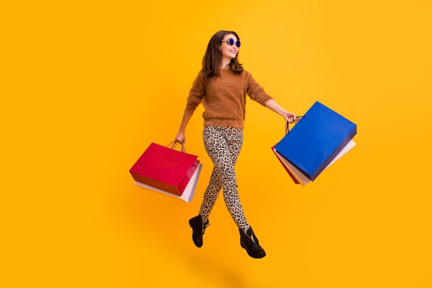 Foto de cuerpo entero de elegante dama saltando alto llevar muchas bolsas de compras