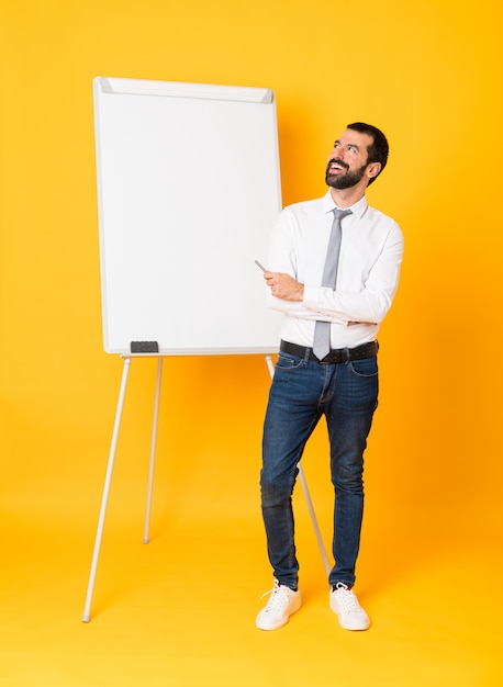 Foto de cuerpo entero del empresario dando una presentación en la pizarra sobre fondo amarillo aislado feliz y sonriente