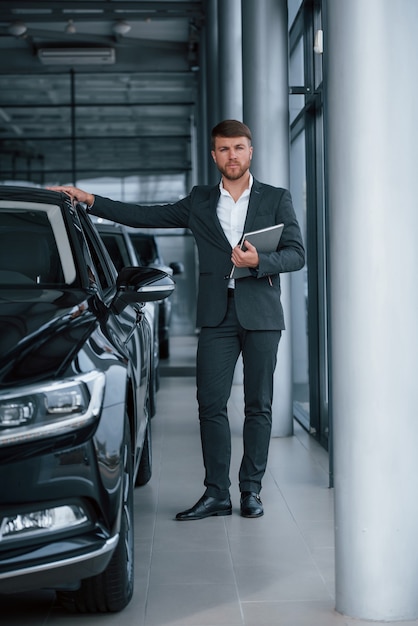 Foto de cuerpo entero. Hombre de negocios barbudo con estilo moderno en el salón del automóvil.