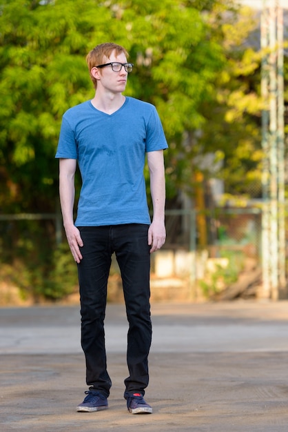 Foto de cuerpo entero de hombre nerd con pelo rojo pensando en el parque