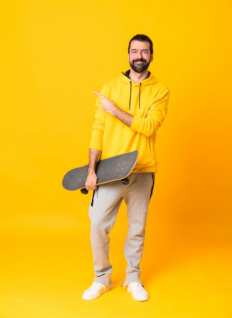 Foto de cuerpo entero del hombre sobre fondo amarillo aislado con un patín y apuntando hacia un lado