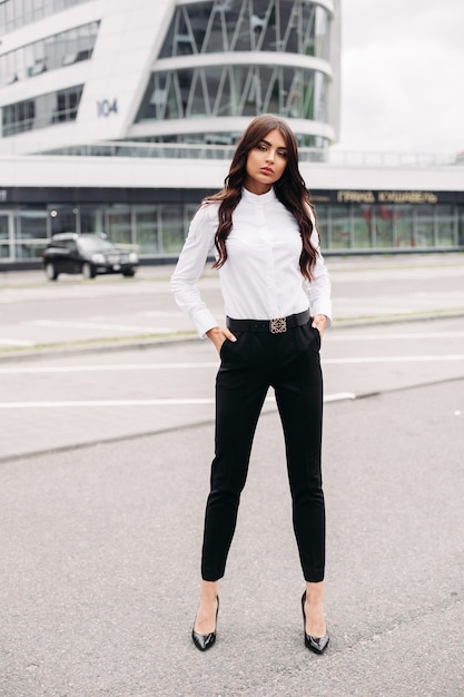 Shetland Hamburguesa escribir Foto de cuerpo entero de una mujer elegante vestida con pantalón negro y camisa  blanca y de pie en la calle frente al edificio moderno. concepto de estilo  y moda | Foto