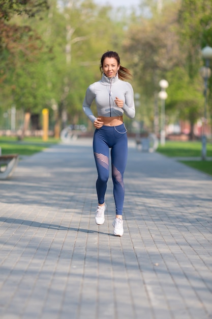 Foto de cuerpo entero de una mujer joven corre en el concepto de parque de la ciudad de mantenerse en forma y estilo de vida saludable