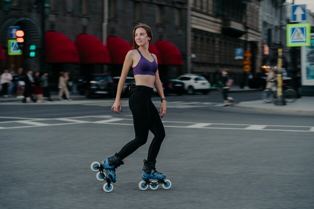 Foto de cuerpo entero de una mujer joven delgada activa vestida con ropa deportiva que se monta sobre rodillos para fortalecer los músculos de los brazos y las piernas, mejora el equilibrio, la agilidad y la coordinación tiene buen humor quema calorías