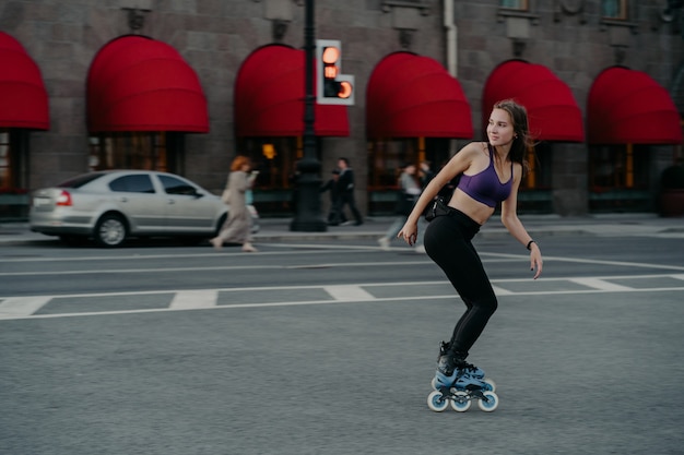 Foto de cuerpo entero de una mujer joven delgada activa vestida con ropa deportiva que se monta sobre rodillos para fortalecer los músculos de los brazos y las piernas, mejora el equilibrio, la agilidad y la coordinación tiene buen humor quema calorías