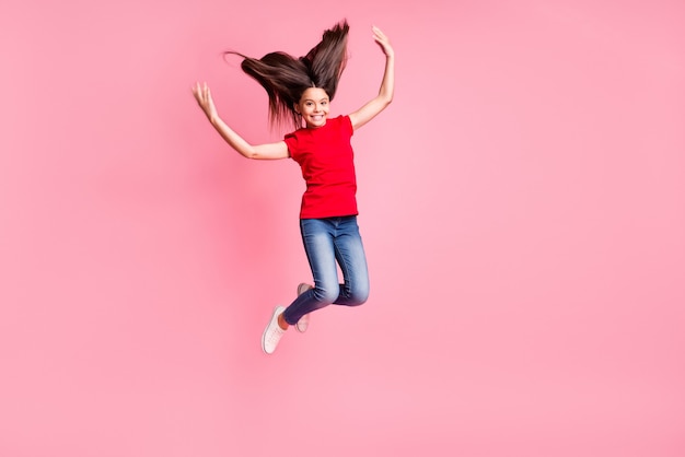 Foto de cuerpo entero de un niño alegre saltando con un peinado largo volando con un atuendo de estilo casual aislado sobre fondo de color pastel
