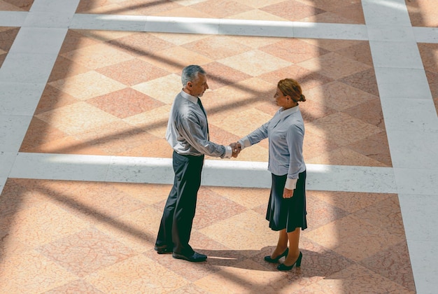 Foto de cuerpo entero de socios comerciales con traje de negocios dándose la mano mientras están de pie en un espacioso salón de oficinas