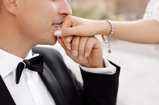 Foto de cultivo de hombre irreconocible en traje de boda besando la mano de su novia en la ternura del vestido de novia, concepto del día de la boda.