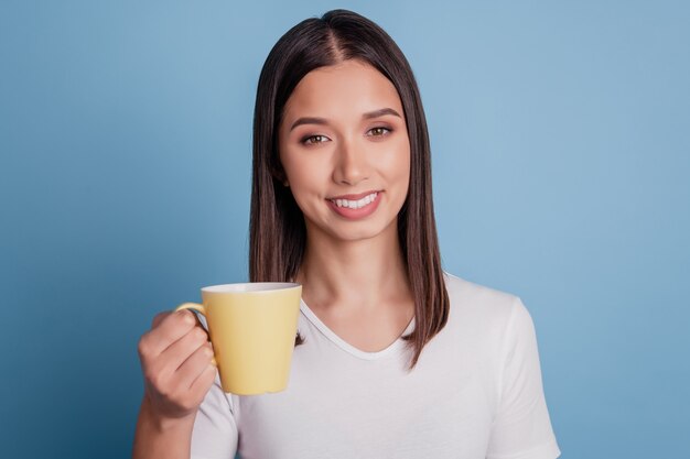 Foto da adorável senhora alegre dos sonhos segurando uma caneca, beber um café sobre fundo azul