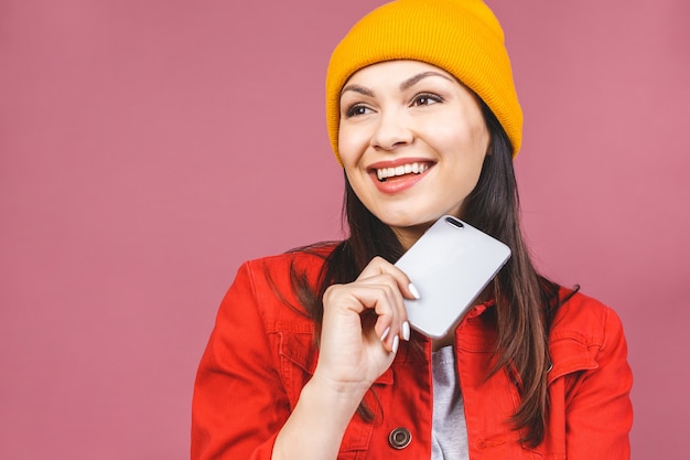 Foto da jovem mulher bonita bonito alegre com o telefone móvel isolado sobre a parede cor-de-rosa da parede.