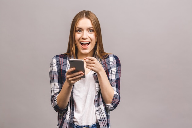 Foto da jovem mulher bonita bonito alegre que conversa pelo telefone móvel isolado sobre a parede cinzenta da parede.