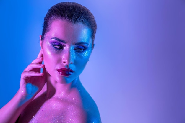 Foto da linda modelo morena no estúdio com filtros de cor Brilho de beleza da moda Rosto aproximado de uma linda mulher morena em neon claro roxo e azul