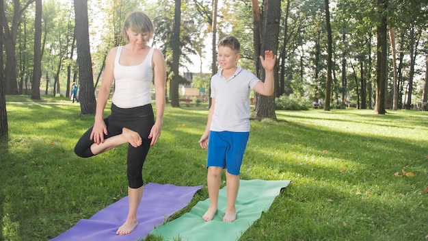 Foto da mãe com seu filho adolescente praticando ioga asana na grama no parque. família fazendo exercícios e praticando esportes na floresta