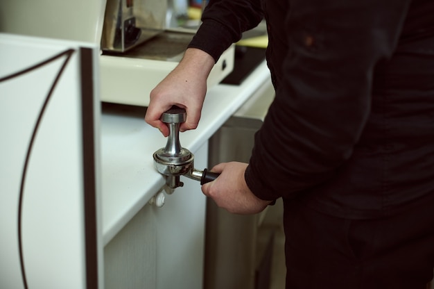 Foto da mão do barista segurando um sabonete líquido e fazendo o preparo do café