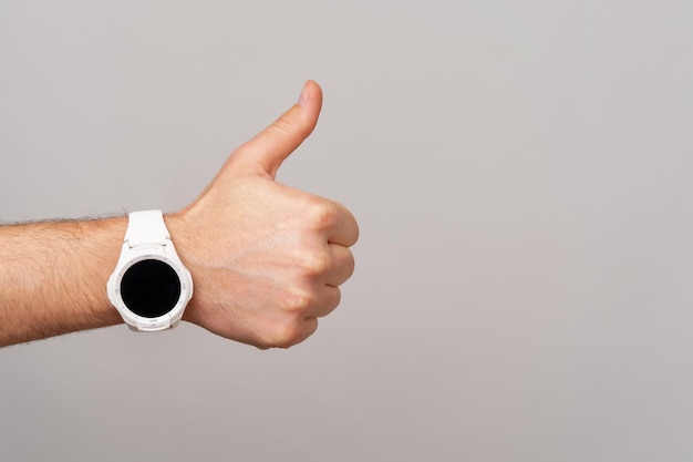 Foto da mão masculina com smartwatch mostrando o polegar para cima gesto sobre fundo cinza