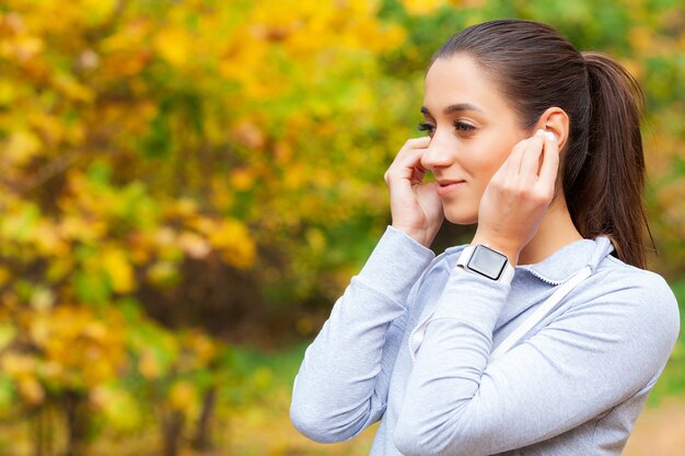 Foto da mulher alegre Fitness 30 anos no Sportswear tocando Bluetooth Earpod e segurando o telefone móvel, enquanto descansava no parque verde