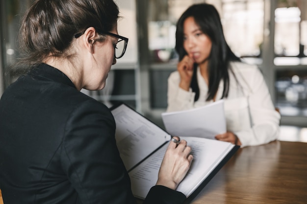 Foto foto da parte de trás de uma mulher de negócios séria entrevistando e conversando com funcionários femininos tensos durante a entrevista de emprego - conceito de negócio, carreira e colocação