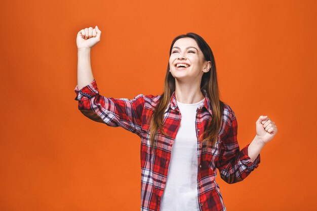 Foto da posição alegre da jovem mulher isolada sobre o fundo alaranjado da parede. Mostrando o gesto do vencedor.