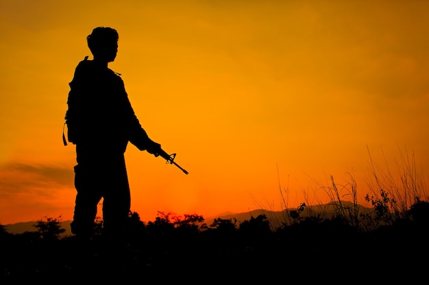 Foto da silhueta de um soldado segurando uma arma com um céu colorido e uma montanha no fundo