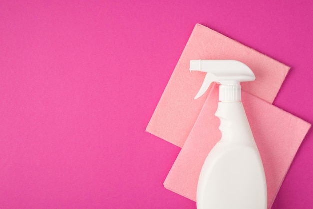 Foto da vista superior do frasco de detergente em spray branco sem rótulo e dois panos de viscose rosa pastel em fundo rosa isolado com copyspace