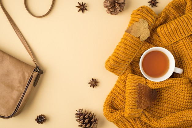 Foto da vista superior do saco de couro xícara de chá outono folhas marrons suéter amarelo anis e pinhas em fundo laranja pastel isolado com copyspace