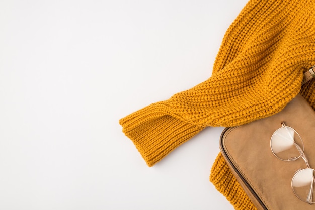 Foto da vista superior do suéter laranja e óculos elegantes na bolsa de couro em fundo branco isolado com espaço para cópia