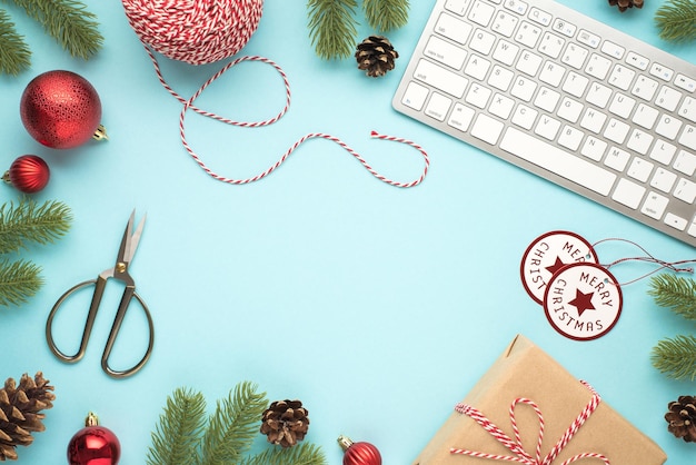 Foto da vista superior do teclado galhos de pinho cones árvore de natal vermelha bolas tesoura carretel de corda decorativa feliz natal tags e caixa de presente de papel artesanal em fundo azul pastel isolado com copyspace