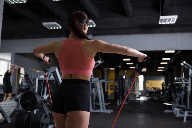 Foto da vista traseira de uma esportista fazendo exercícios para os ombros com faixa de resistência, copie o espaço