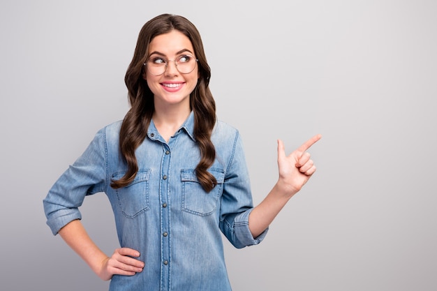 Foto de dama de negocios bastante divertido indicar el dedo espacio vacío asesorar a los compradores de productos novedosos mirar hacia el lado especificaciones de desgaste casual jeans camisa de mezclilla color gris aislado