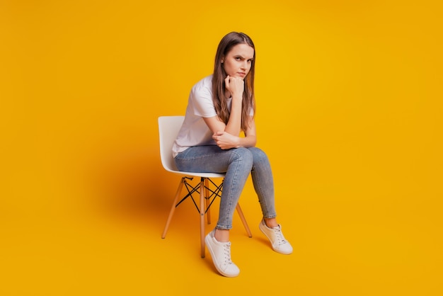 Foto de dama sentarse sillón puño barbilla cara enojada usar camiseta blanca posando sobre fondo amarillo