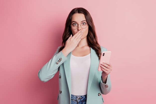 Foto foto de dama sorprendida sostenga la boca de la cubierta de la palma del teléfono posando sobre fondo rosa