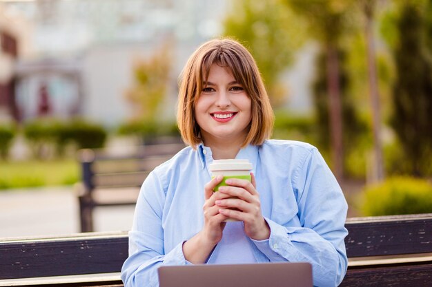 Foto de adorável jovem bonita vestindo camisa azul bebendo chá e café fora da rua urbana