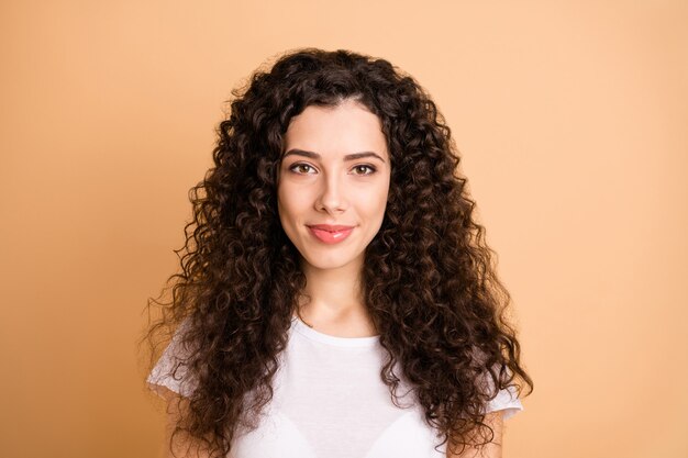 Foto de alegre positiva fofa doce garota olhando para você com o cabelo encaracolado isolado sobre um fundo bege