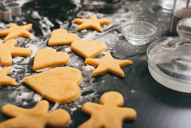 Foto de algumas figuras de pão de gengibre não assado em uma mesa preta com um pouco de farinha.